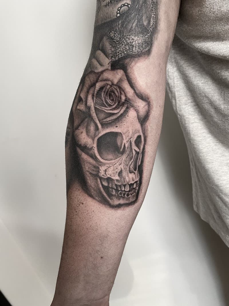 Realistische schedel met roos tattoo op onderarm.