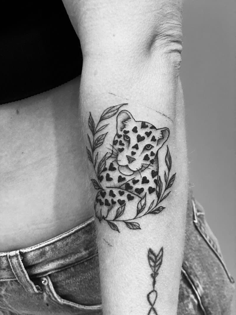 Zwart-wit tattoo van een luipaardwelp met hartjesvlekken en bladeren.
