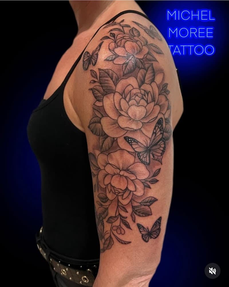 Zwart-wit tattoo van pioenrozen en vlinders op de bovenarm.