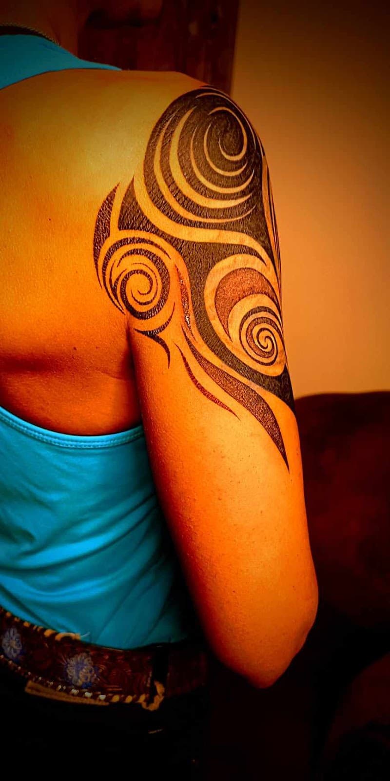 Zwarte tribal tattoo met spiralen op bovenarm en schouder.