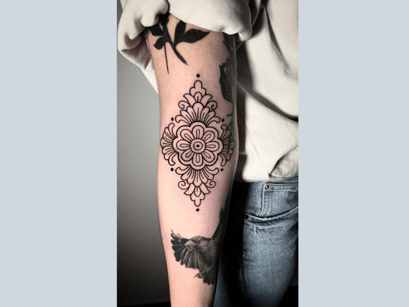 Ornamentale mandala tattoo met bloemmotief op de achterkant van de bovenarm.