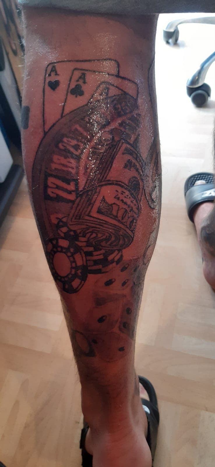 Gokthema tattoo met kaarten, roulette, geld en dobbelstenen op onderbeen.