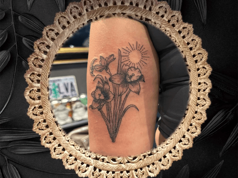 Fineline tattoo van narcissen met een zon en maan op de bovenarm.