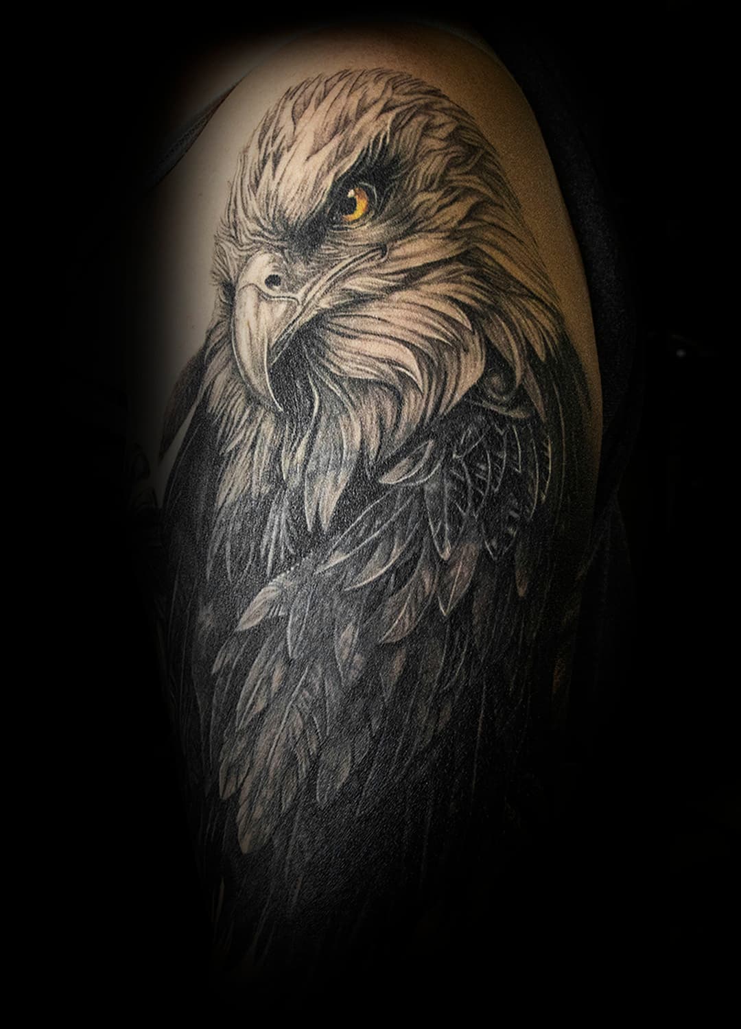 Realistische zwart-wit adelaar tattoo met geel oog op bovenarm.