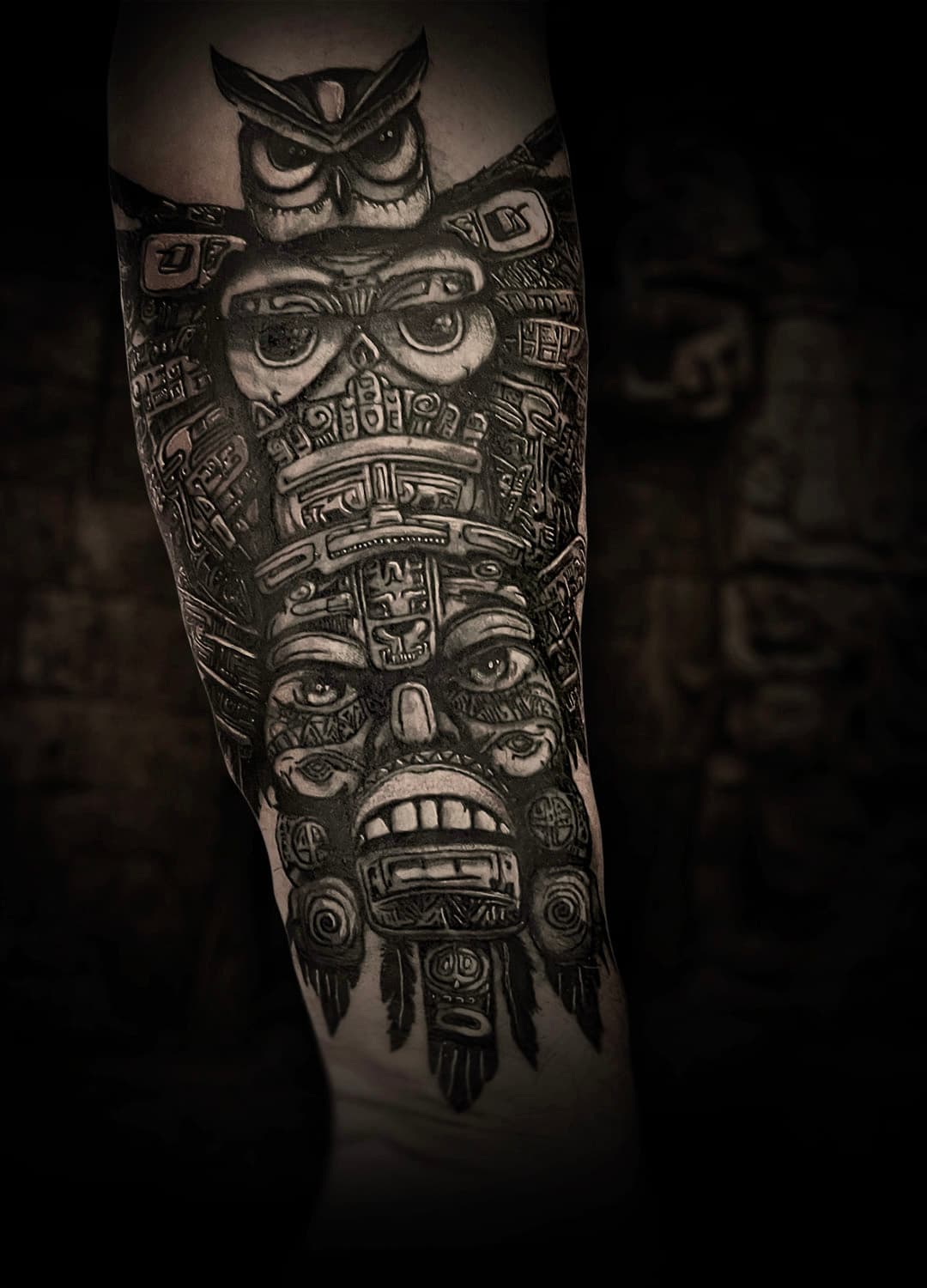 Gedetailleerde zwart-wit Maya/Azteekse totempaal tattoo op de bovenarm.