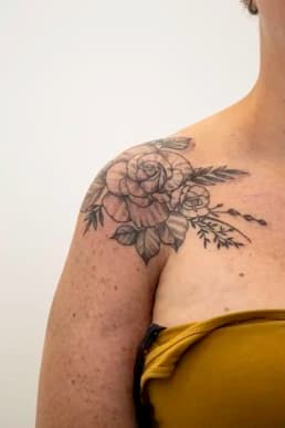 Blackwork bloemen tattoo op schouder met rozen en bladeren.