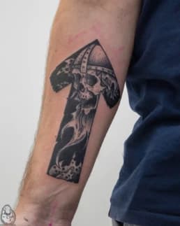 Zwart-wit tattoo van een schedel met helm in een pijl op de onderarm.