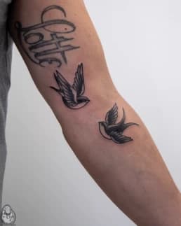 Drie tattoos op de bovenarm: de naam 'Lotte' en twee zwaluwen.