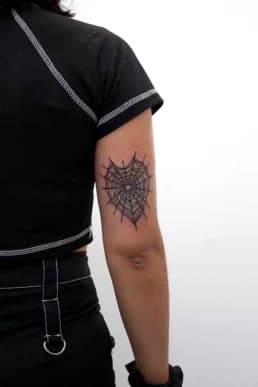 Zwartwerk spinnenweb tattoo in hartvorm op de achterkant van de bovenarm.