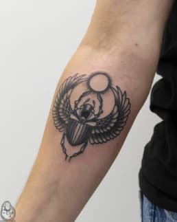 Zwart-wit scarabee tattoo met vleugels en zon op de onderarm.