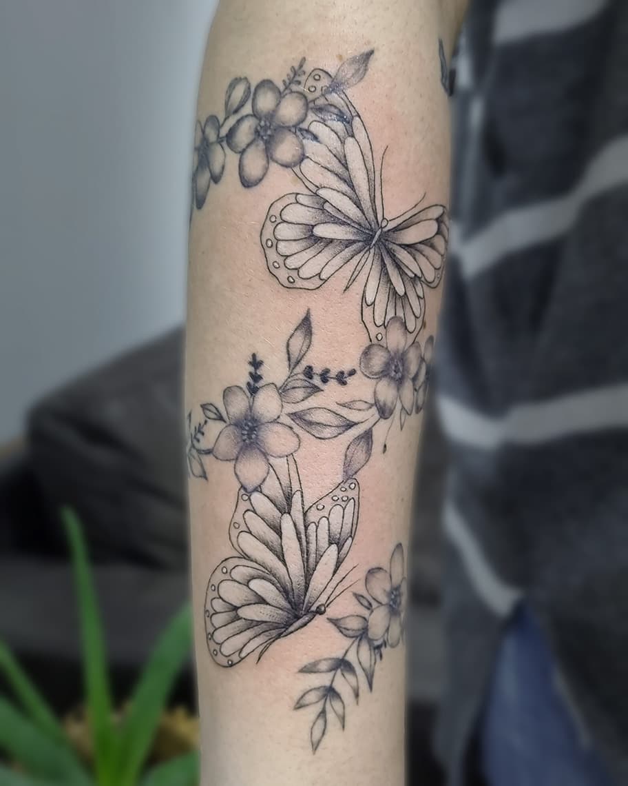 Fineline tattoo van vlinders en bloemen op de onderarm.