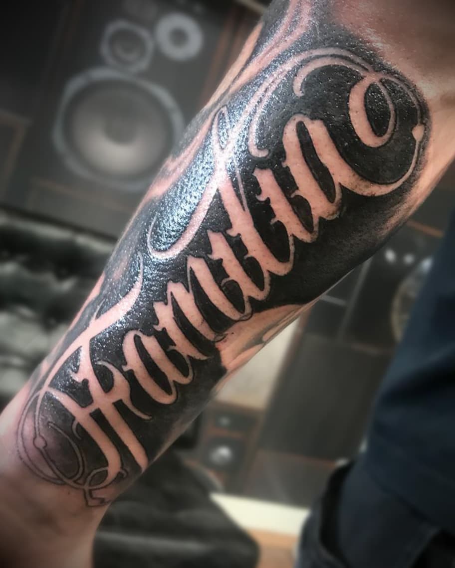Grote 'Familia' tekst tattoo in sierlijk script op de onderarm.