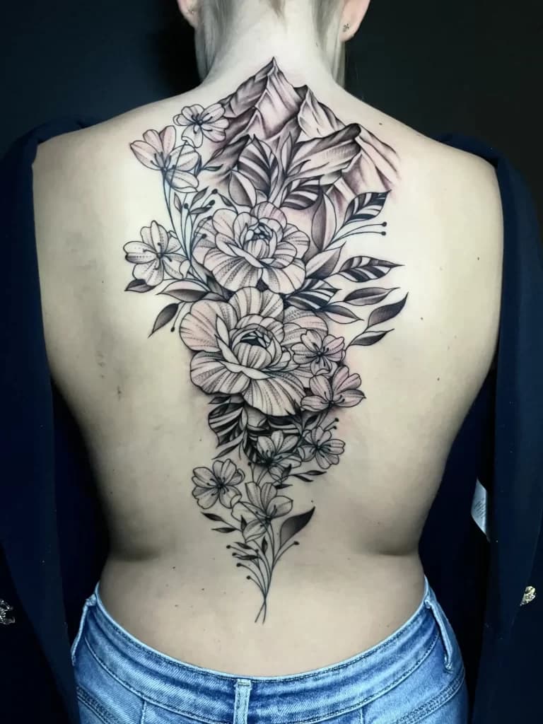 Grote fineline tattoo van bloemen en bergen op de rug.
