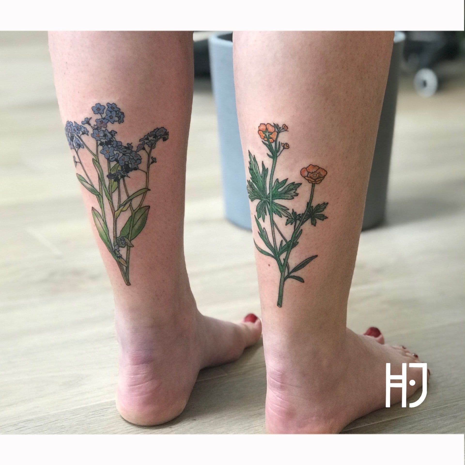 Twee botanische tattoos van vergeet-mij-nietjes en boterbloemen op de kuiten.