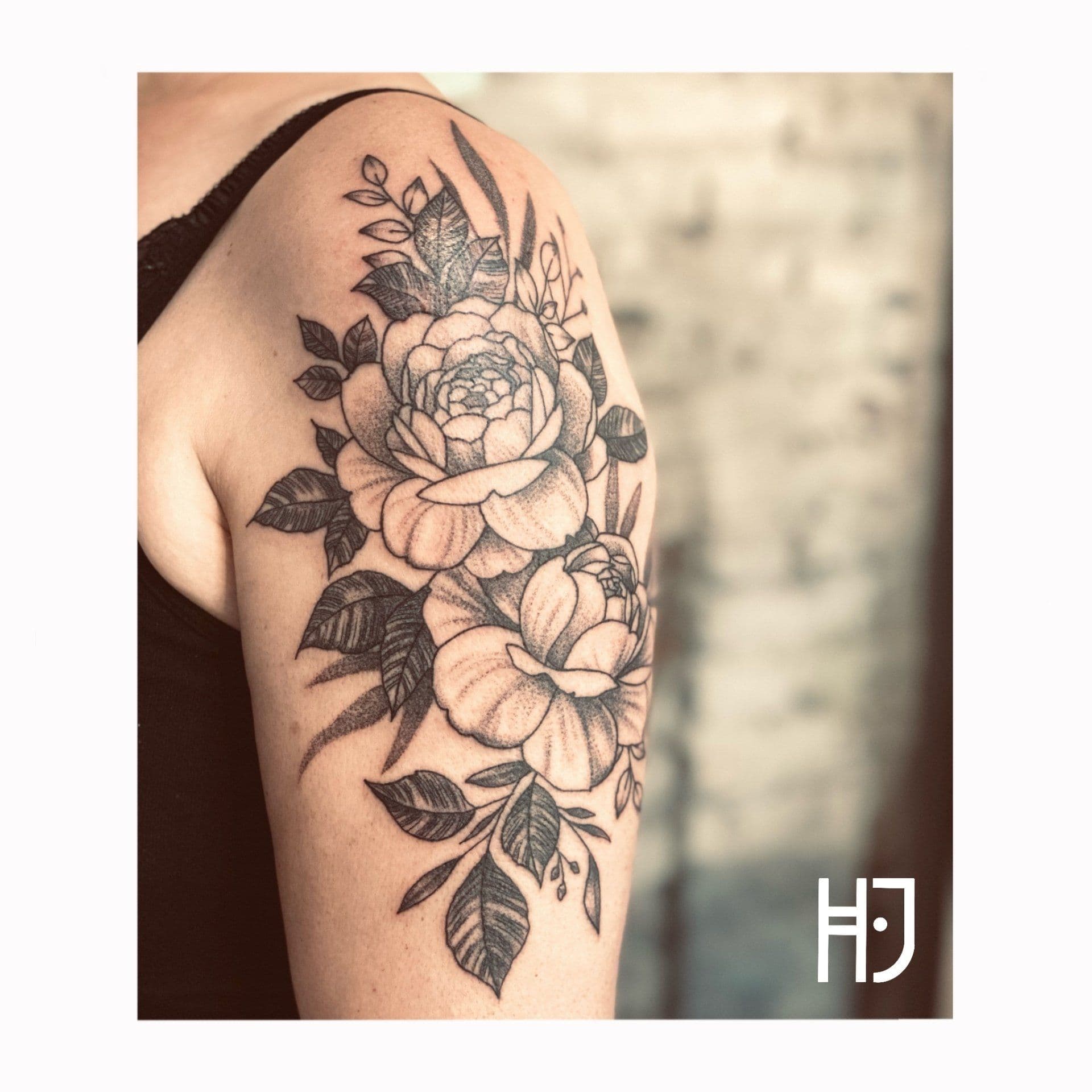 Zwart-wit dotwork tattoo van pioenrozen en bladeren op de bovenarm.