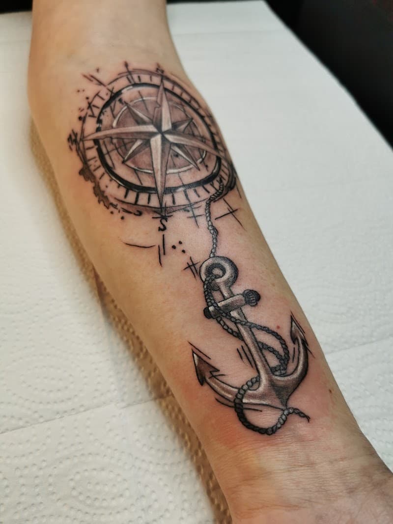 Kompasroos en anker tattoo in schetsstijl op onderarm.
