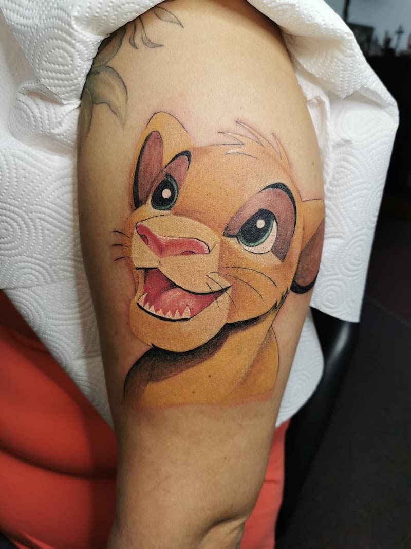 Kleurrijke tattoo van Simba uit de Leeuwenkoning op de bovenarm.