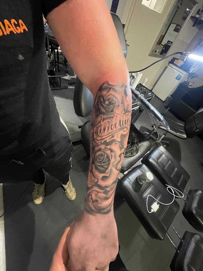 Zwart-grijze tattoo van rozen en 'Familia' tekst op de onderarm.