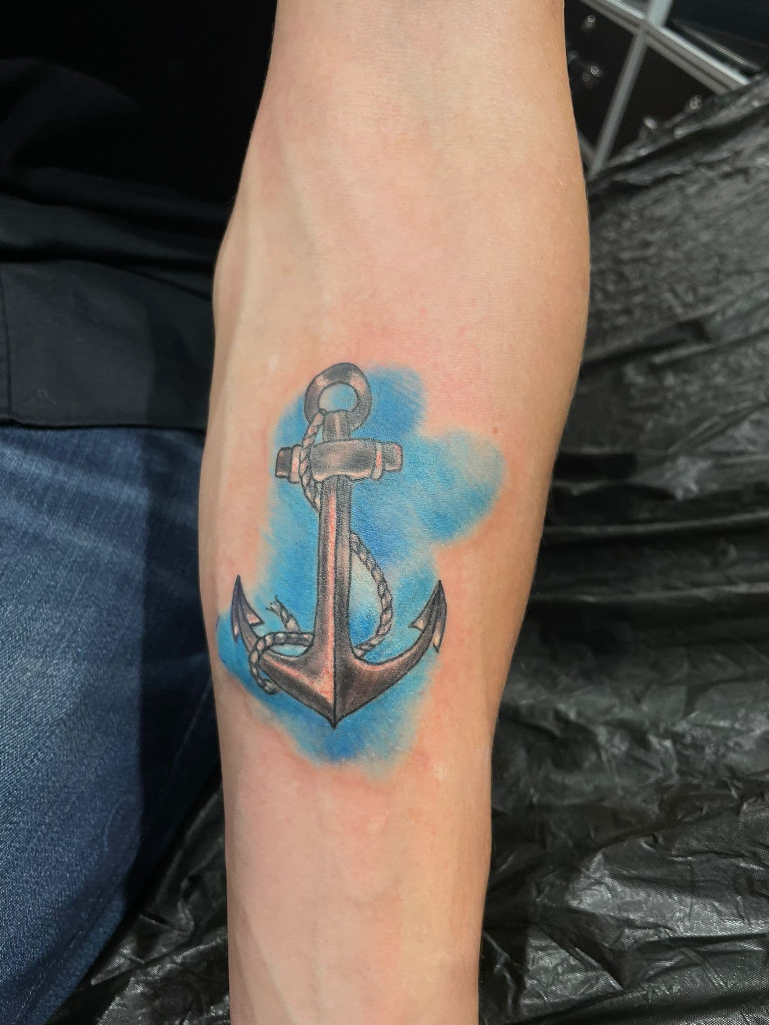 Anker met touw en blauwe aquarel achtergrond op onderarm.