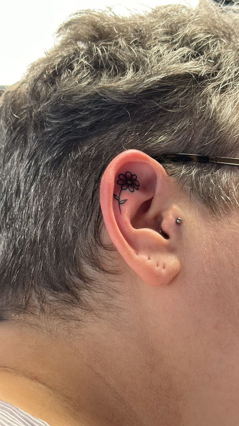 Kleine bloem tattoo met rode blaadjes in de oorschelp.