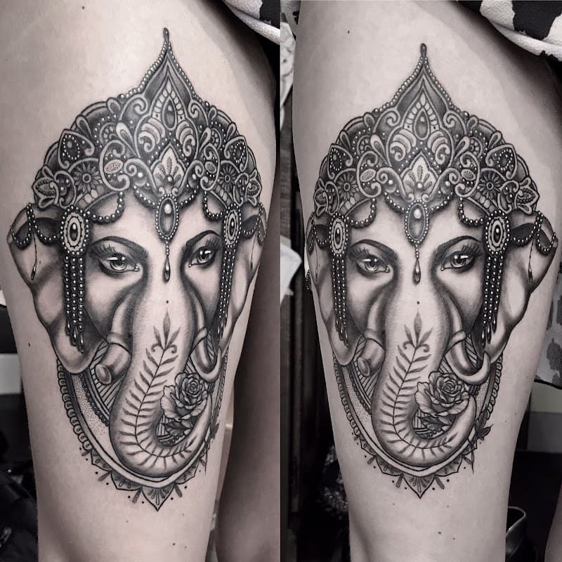 Zwart-wit Ganesha tattoo met sierlijke kroon en roos op bovenbeen.