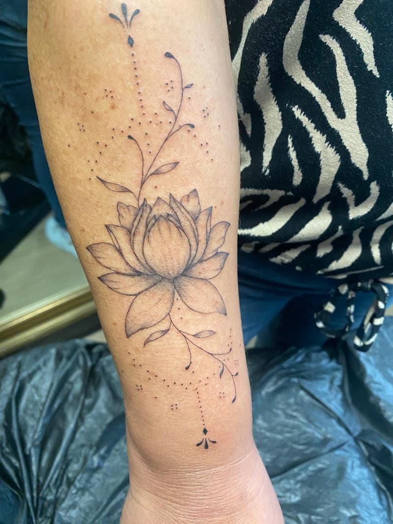 Fineline lotusbloem met sierlijke takjes en stippen op de onderarm.