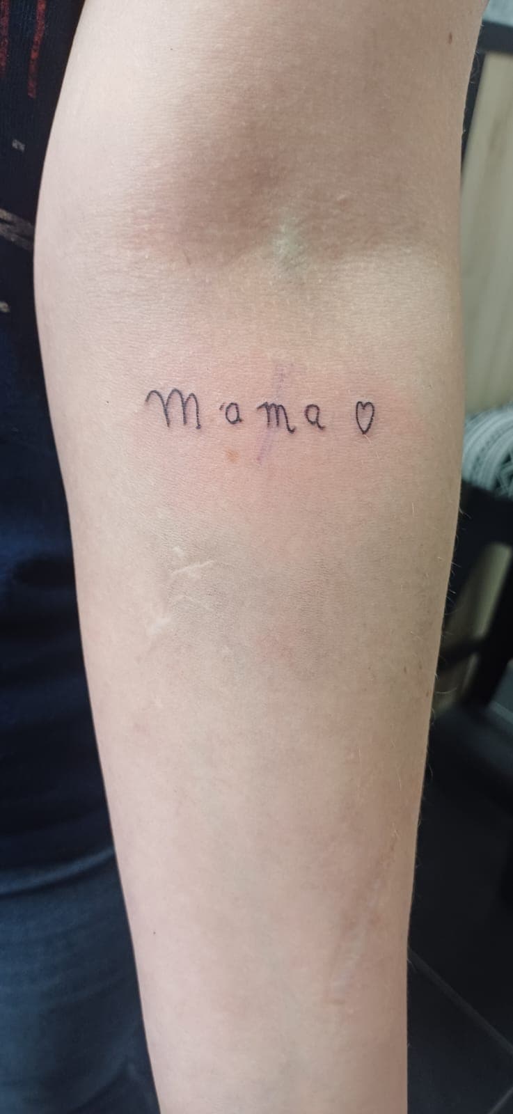 Fineline tattoo van het woord 'mama' met een hartje op de onderarm.