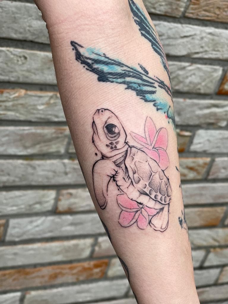 Fineline tattoo van een schildpad met roze bloemen op de onderarm.