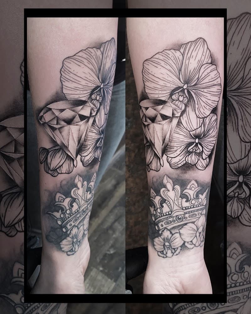 Zwart-wit tattoo van een diamant, orchideeën en een kroon op de onderarm.