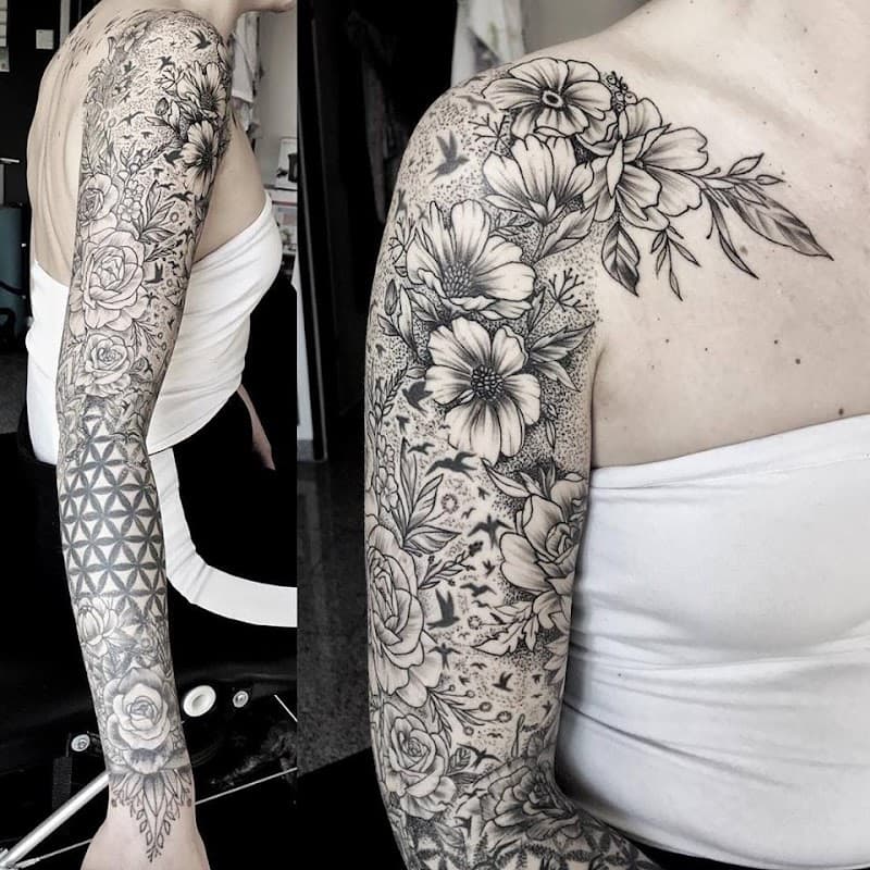 Blackwork sleeve met bloemen, vogels en geometrisch patroon.