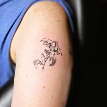 Kleine fineline bloem met gezichtje op bovenarm