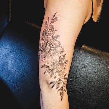 Fineline bloemen tattoo met bladeren op de bovenarm.
