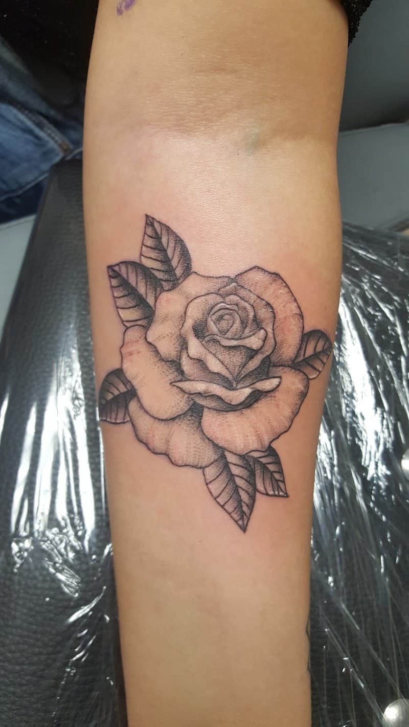 Zwart-wit roos tattoo met bladeren op de onderarm.