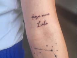 Fineline tekst 'diese eine Liebe' en sterrenbeeld op bovenarm.