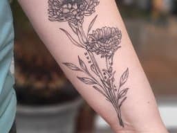 Fineline tattoo van twee anjers met initialen op de onderarm.