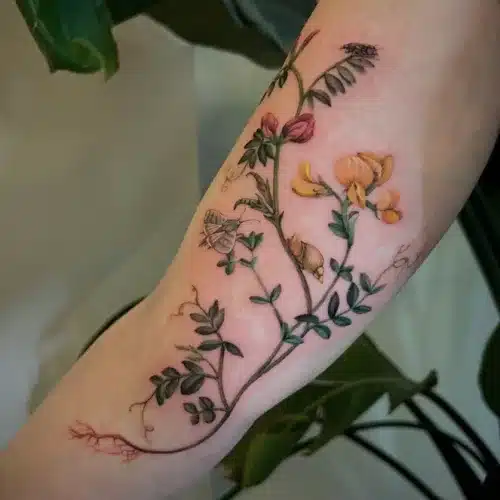 Botanische tattoo met bloemen, bladeren, een mot en een slak op de arm.