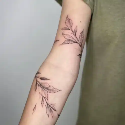 Fineline tattoo van bladeren en takken die om de arm wikkelen.