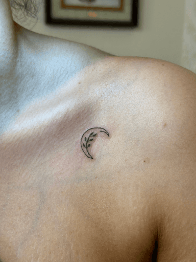 Minimalistische halve maan met takje en blaadjes op het sleutelbeen.