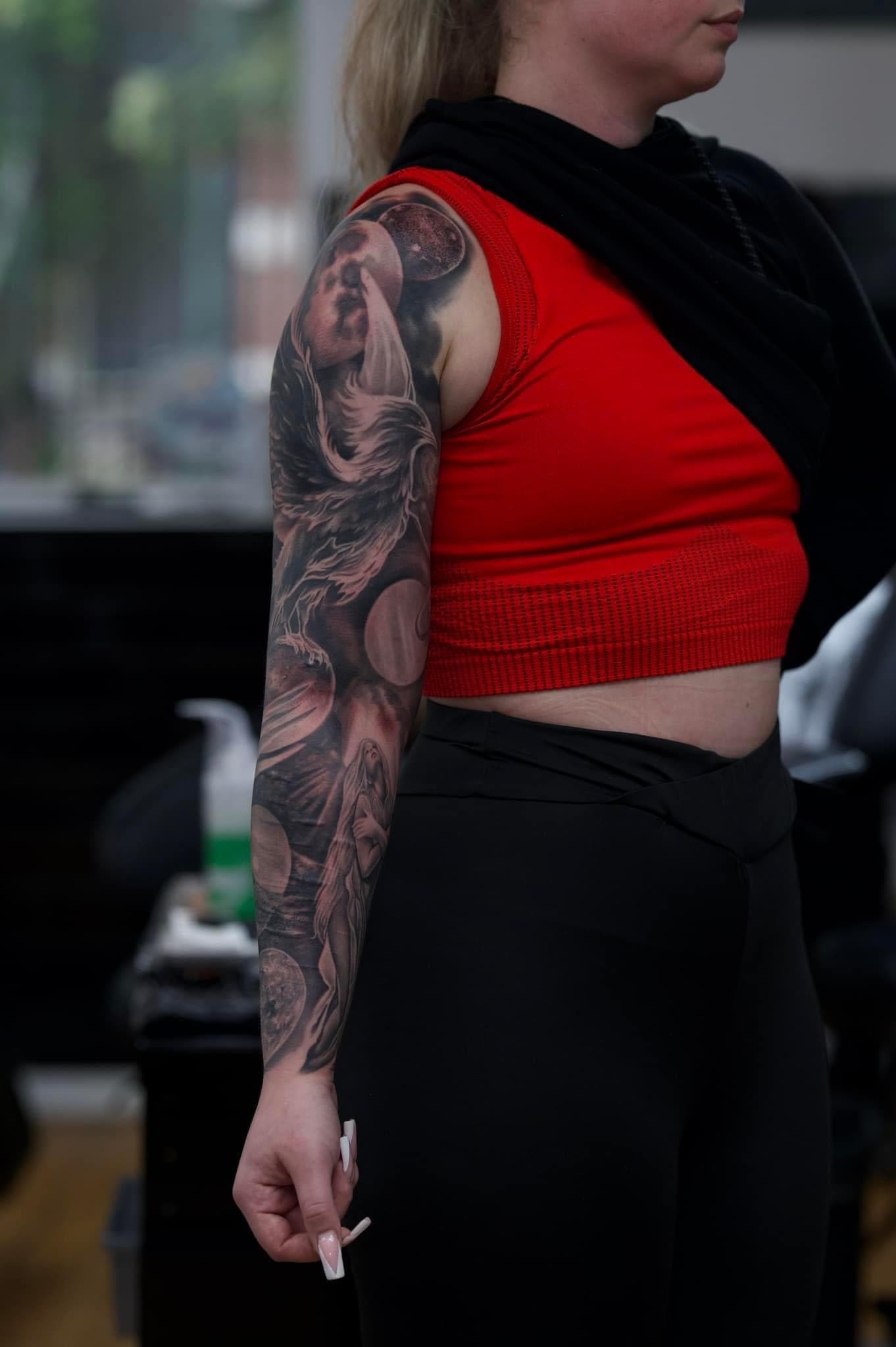 Volledige sleeve tattoo met feniks, planeten en een vrouwenfiguur in zwart-wit.