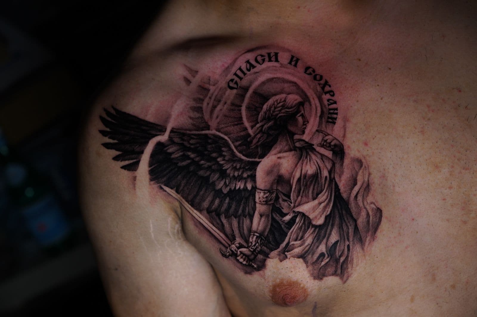 Realistische zwart-wit tattoo van een engel met zwaard en Russische tekst.
