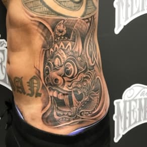 Grote zwart-wit Barong masker tattoo op de zij.
