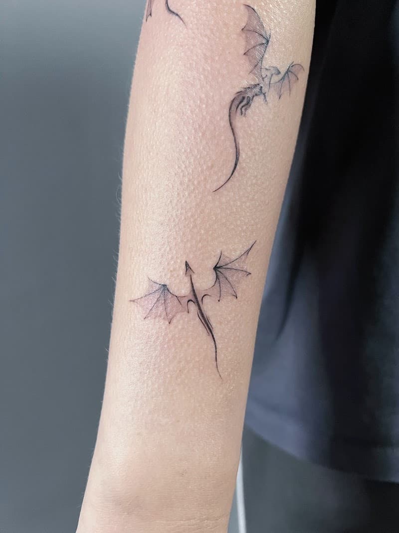 Twee fineline draak tattoos op onderarm.
