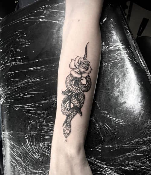 Zwart-wit tattoo van een slang die om een roos kronkelt op de onderarm.