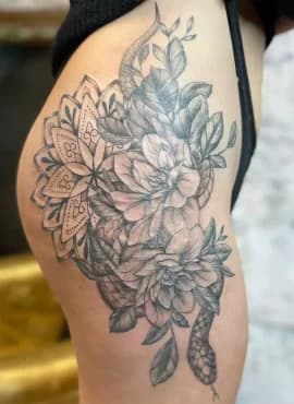 Zwart-wit tattoo van mandala, bloemen en slang op heup.