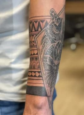 Blackwork tattoo op onderarm met een tribal band en een geometrische uil.