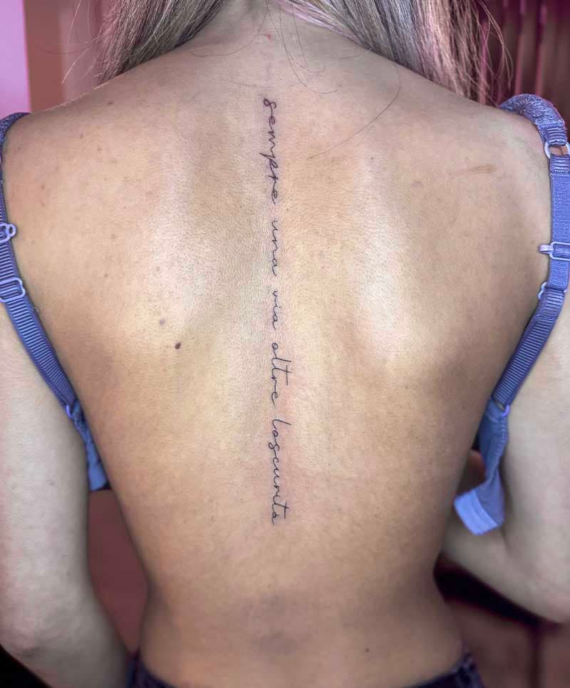 Fineline tekst tattoo 'sempre una via oltre l'oscurità' op de ruggengraat.