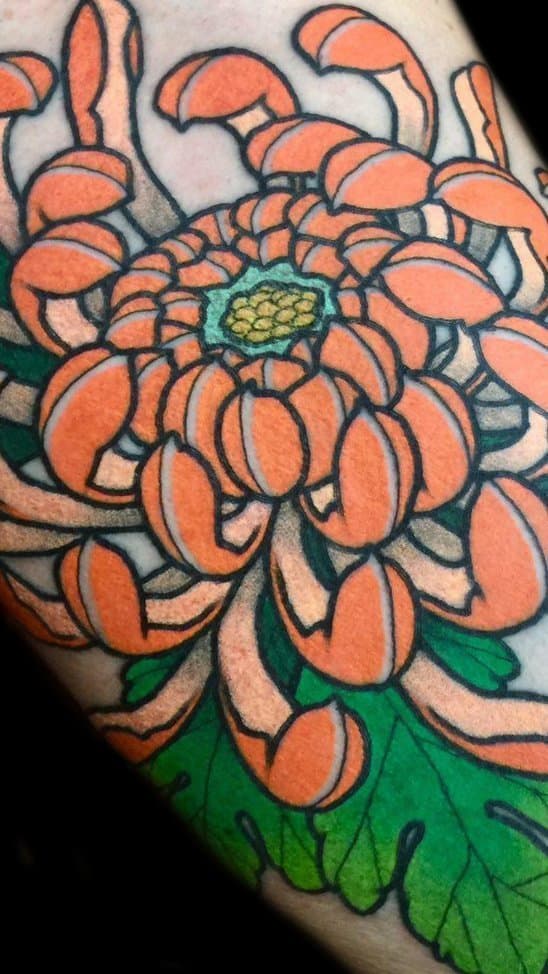 Close-up van een oranje Japanse chrysant tattoo met groene bladeren.