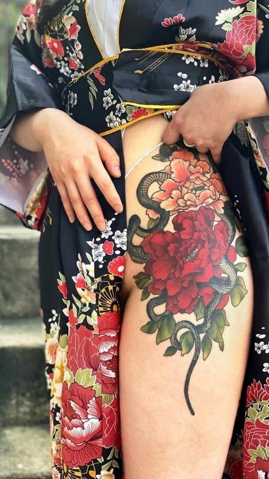 Grote Japanse tattoo van een slang en pioenrozen op de heup.
