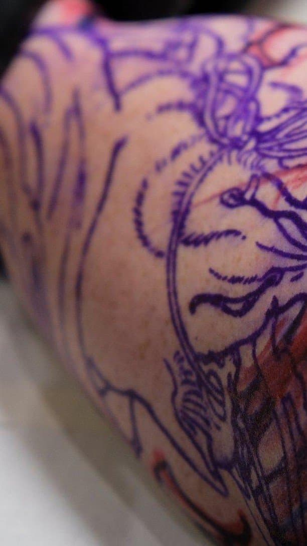 Close-up van een paars tattoo stencil en het begin van een tattoo op een arm.