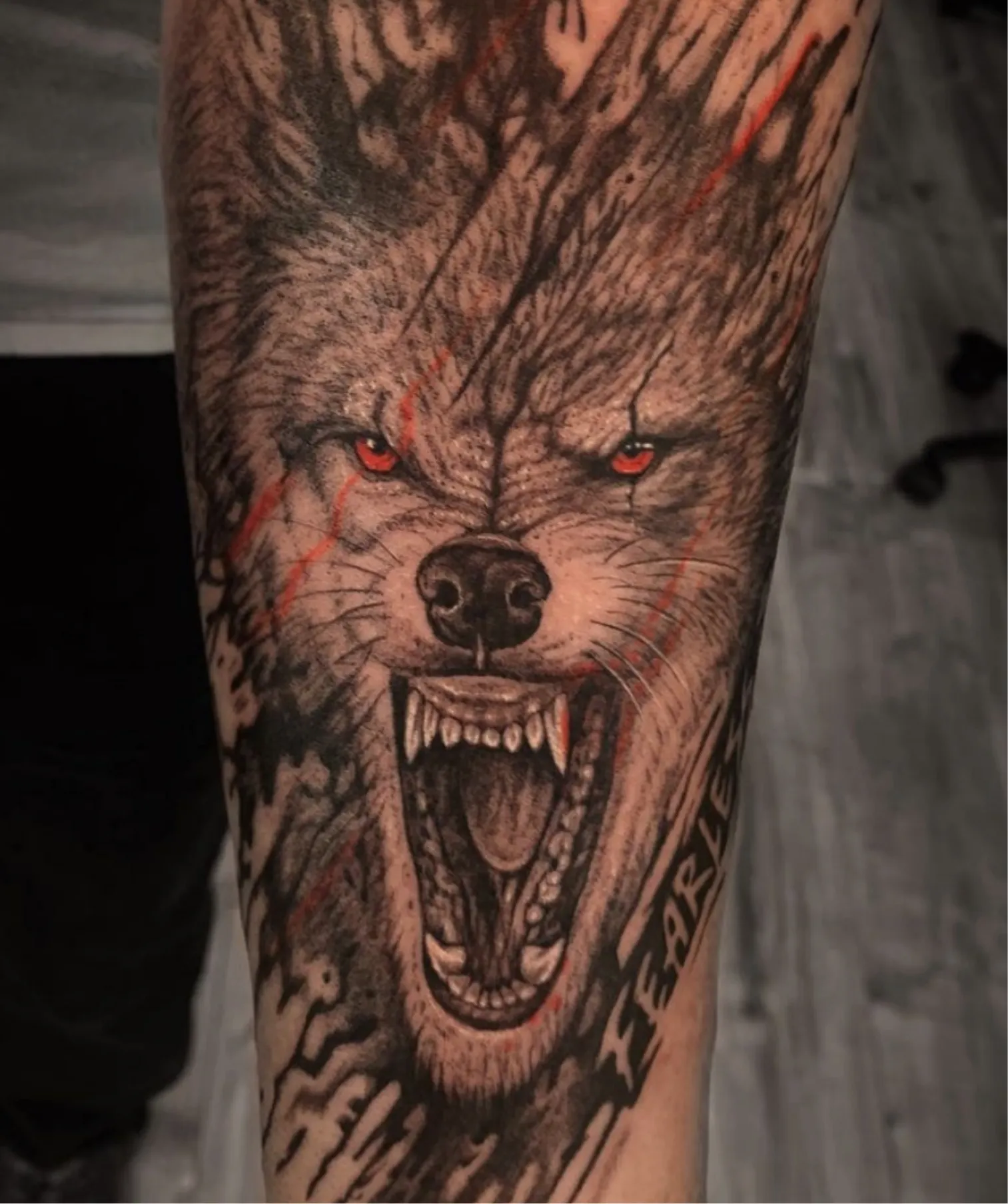 Grommende wolf tattoo met rode ogen, krassen en de tekst 'FEARLESS'.